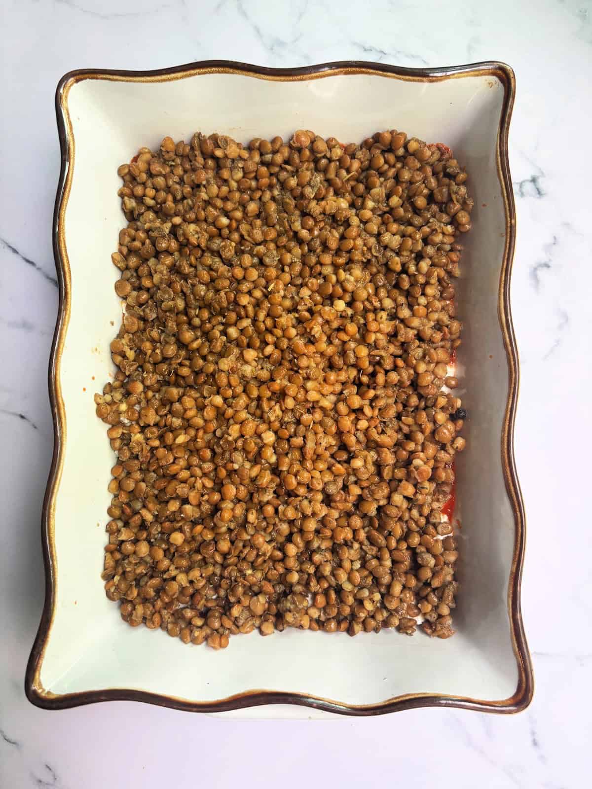 Savory cooked lentils as a layer on abutternut squash lasagna.  gold rimmed baking dish. Perfect for healthy dinner recipes.