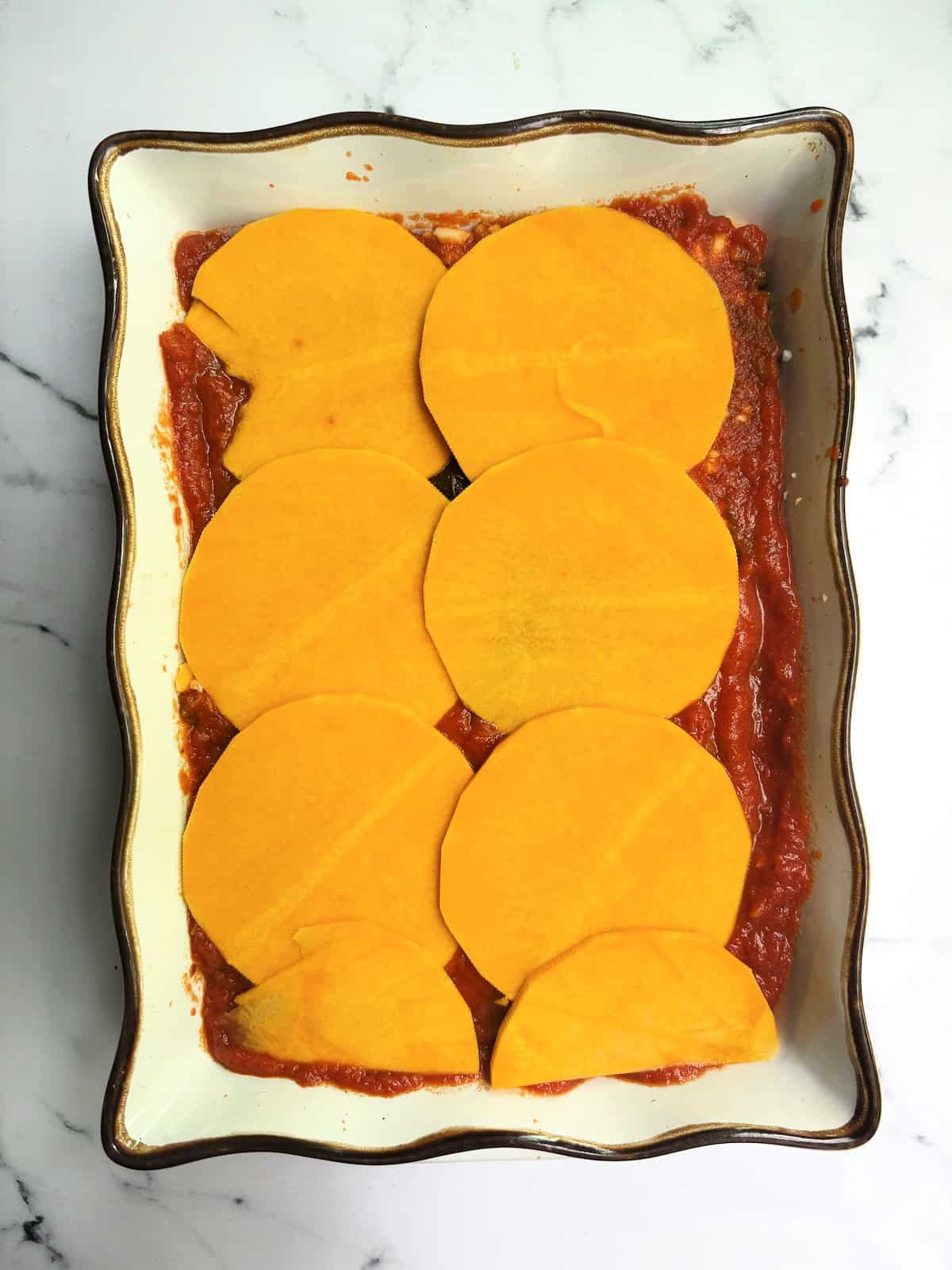 Thin rounds of butternut squash, layered on a lasagna baking dish
